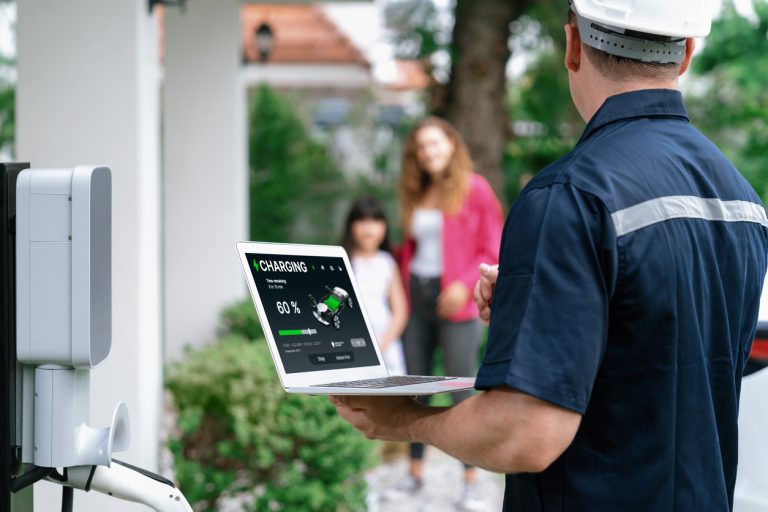 multifamily ai tools Technician in uniform and helmet checks a charging station with a laptop. Charging status shows 60%. Two people stand in the background. mpro Digital Edge
