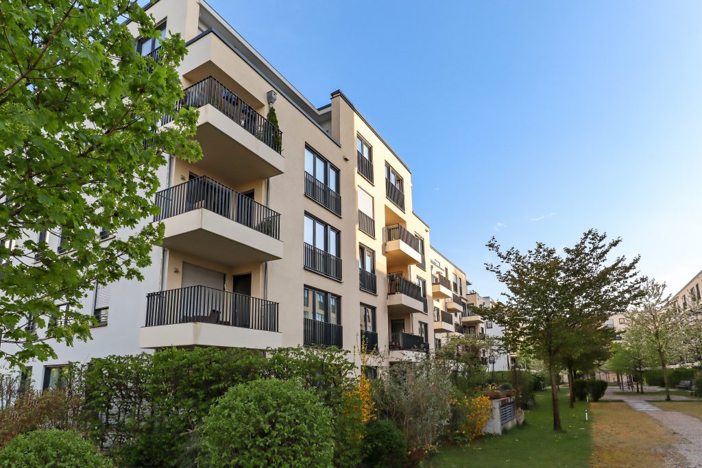 multifamily ai tools Modern apartment building with multiple balconies, surrounded by green shrubs and trees, set against a clear blue sky. mpro Digital Edge